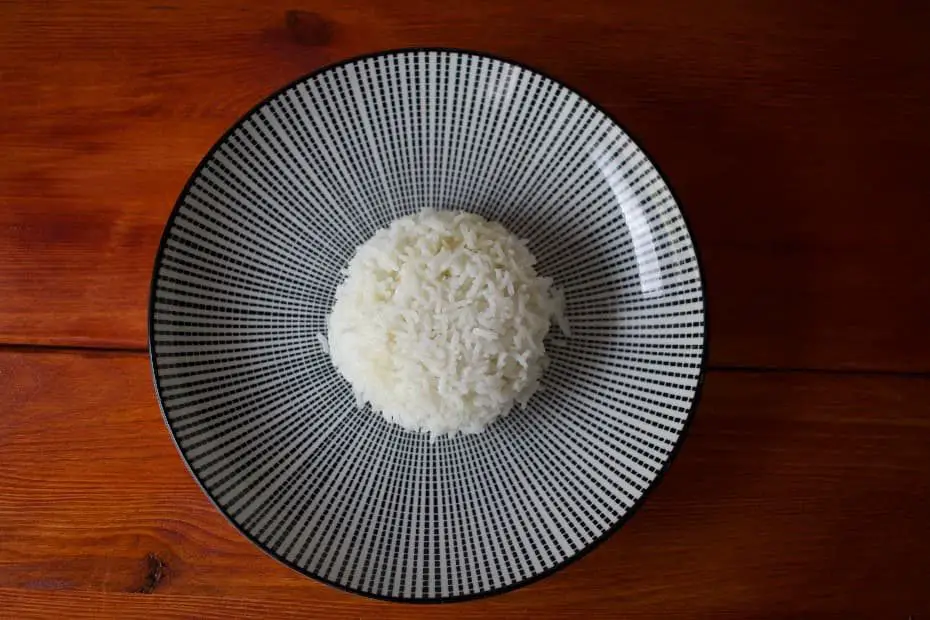 100 Gramm gekochter Reis liegen auf einem Teller