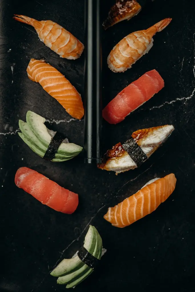 Nigiri Sushi mit Lachs, Thunfisch, Garnele und Avocado liegt auf einem schwarzen Untergrund