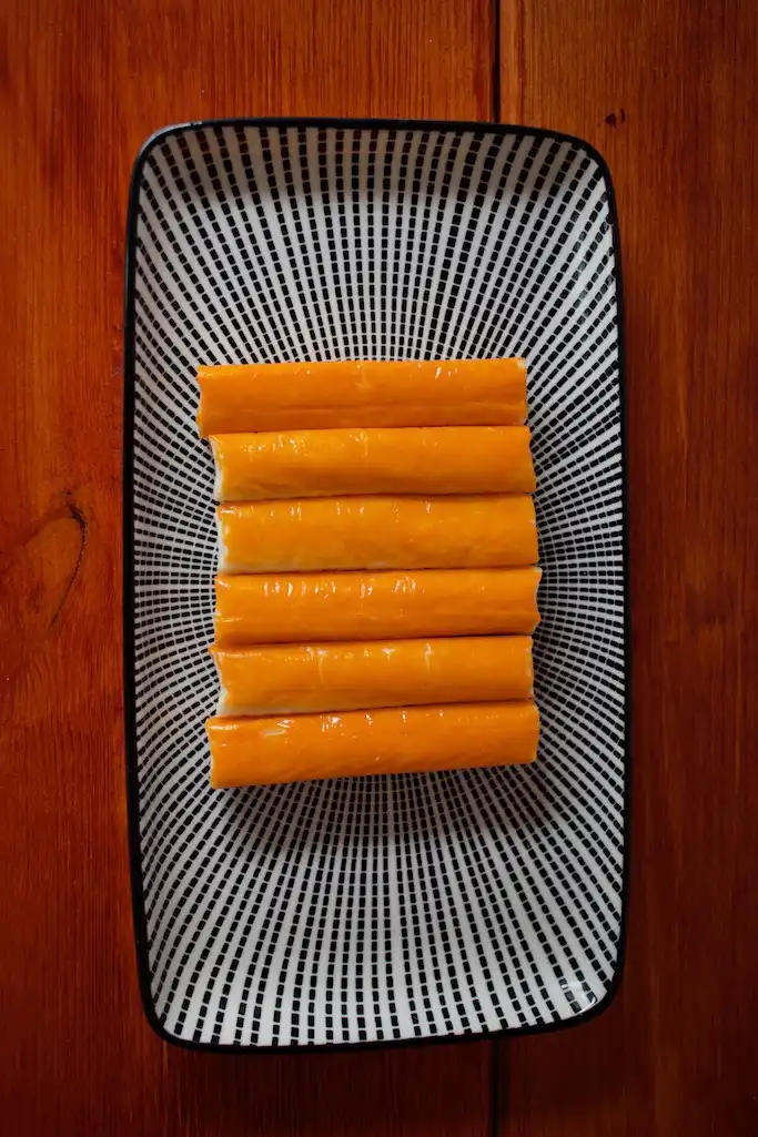 6 Stück Surimi Sticks liegen auf einem schwarz weißen Teller