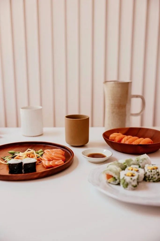 Sushi Geschirr mit Nigiri, Maki,  Uramaki und Porzellantassen stehen auf einem weißen Tisch.