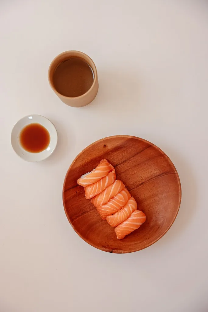 6 Stücke Nigiri Sushi liegen auf einer brauen Holzschale. Daneben steht eine Schale mit Sojasauce.