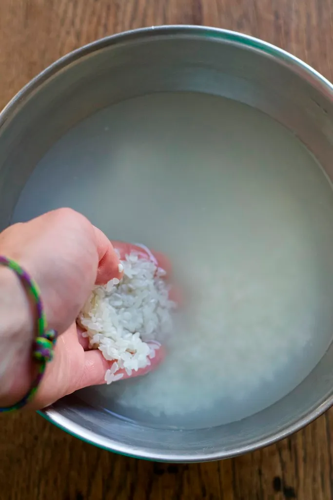 Sushi Reis in einer Metallschale mit Wasser waschen
