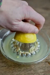 Eine Hand presst eine gelbe Zitrone mit einer Zitronenpresse aus Glas