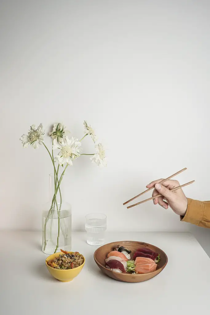 Auf einem Tisch steht eine Teller mit Sushi, ein Glas Wasser und eine Blumenvase