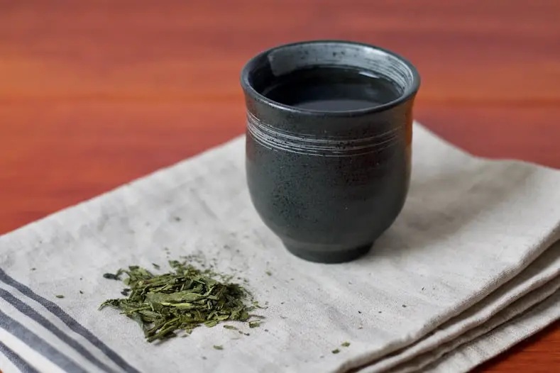 Teeblätter und eine Tasse mit Bancha Tee stehen auf einem Geschirrtuch